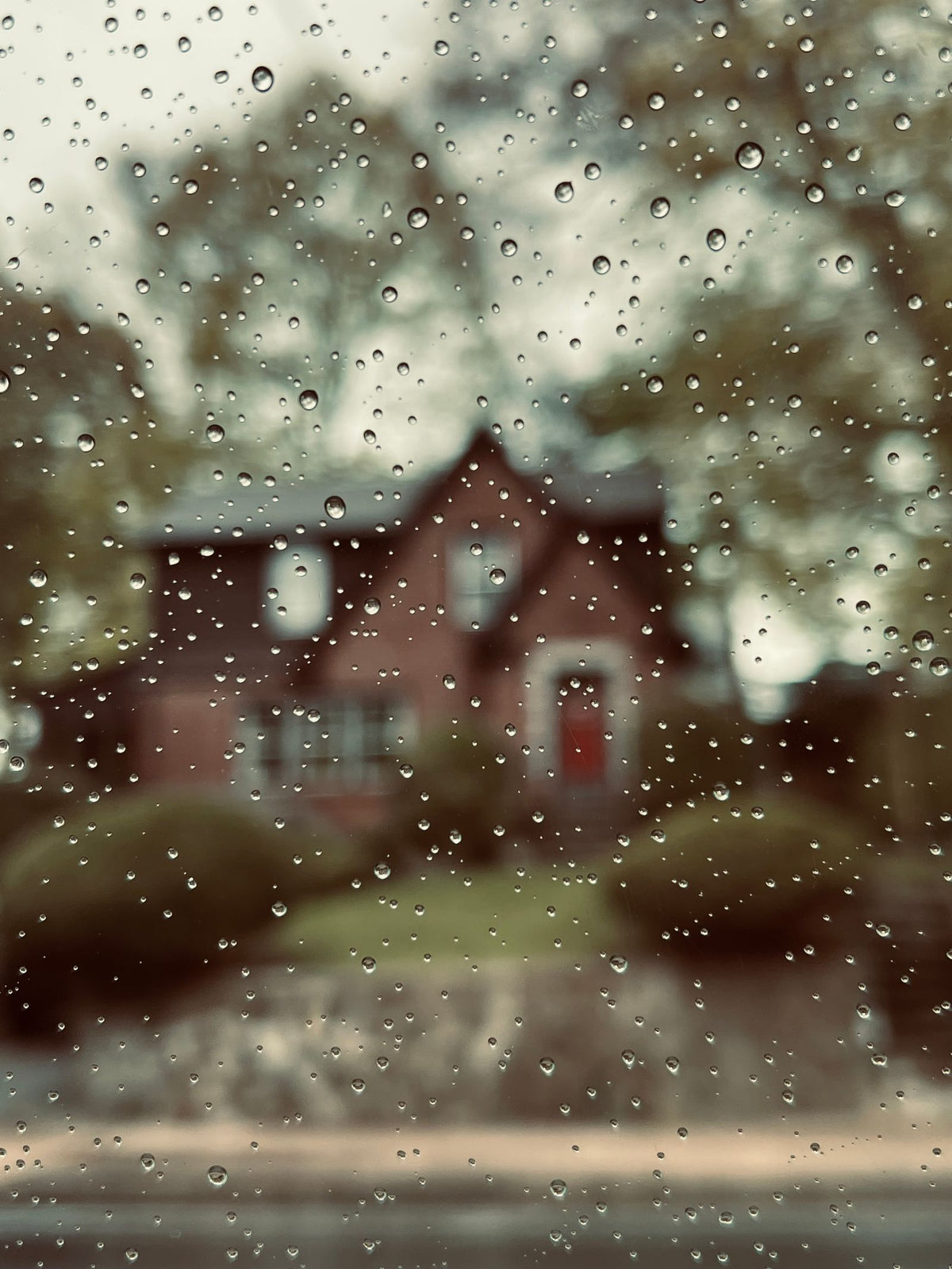 Regendruppels op een raam met een huis op de achtergrond, natte herfstdagen waarop vocht in huis toeneemt