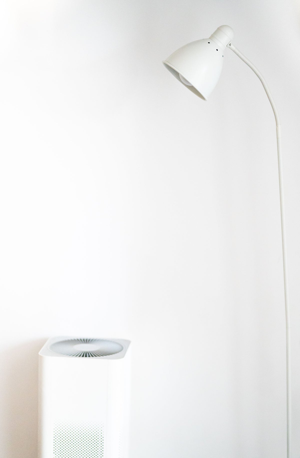 Luchtreiniger naast een witte staande lamp tegen een lichte muur