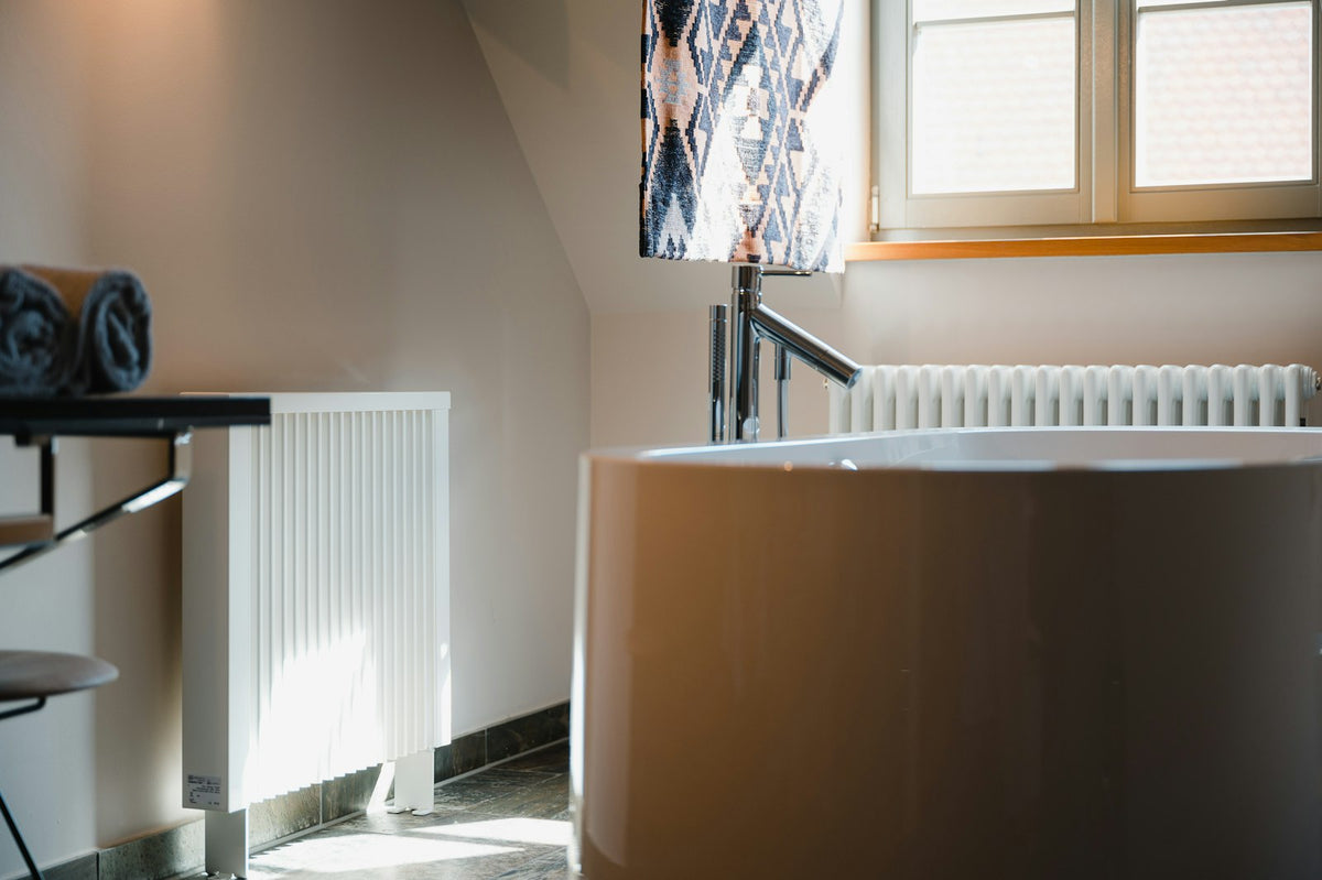 Witte elektrische kachel bij een raam in een kamer, passend bij het stroomverbruik van een kachel
